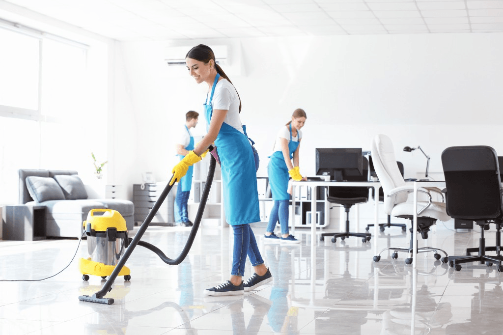 Uniformed cleaning crew vacuuming and wiping down a bright commercial office
