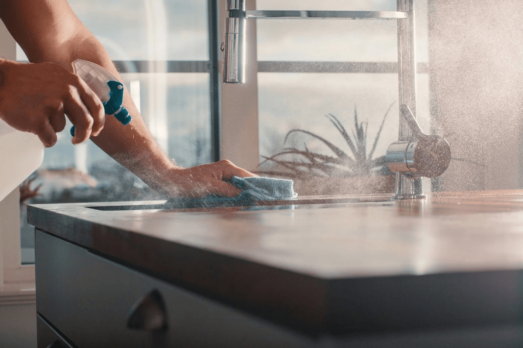 Hands spraying and wiping a kitchen countertop with a microfiber cloth