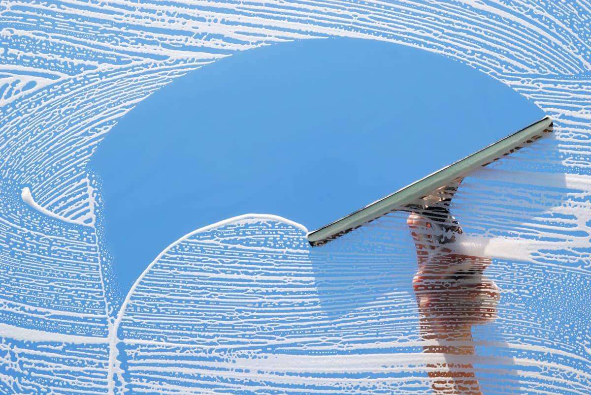 Hand using a squeegee to clean a soapy window